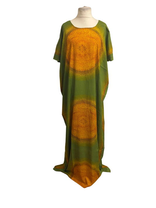 A long, loose kaftan dress displayed on a mannequin in front of a white fabric backdrop. The dress has a green base with large circular mandala-like patterns in yellow and orange.