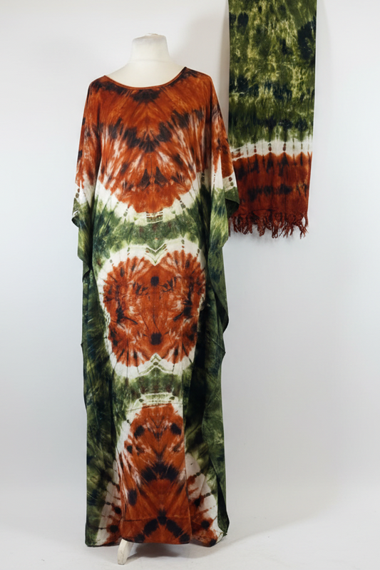 A long kaftan dress with a tie-dye pattern in rust orange, green, and white, displayed on a mannequin against a white studio background, with a matching scarf hanging on the right.