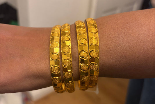 Gold bracelets on a wrist with a blurred indoor background