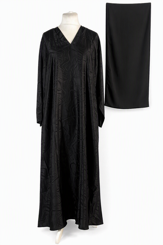 A black long-sleeved maxi abaya dress with a subtle tonal jacquard pattern, displayed on a mannequin next to a matching black skirt on a white background.