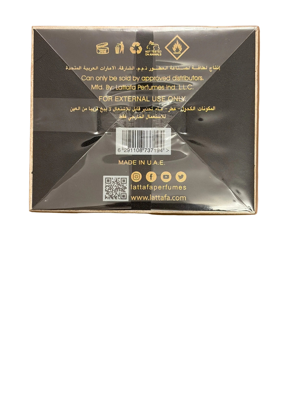 The back of a square black perfume box wrapped in clear plastic, placed on a wooden surface. The box features gold text and symbols, including the brand name 'Lattafa' and website 'www.