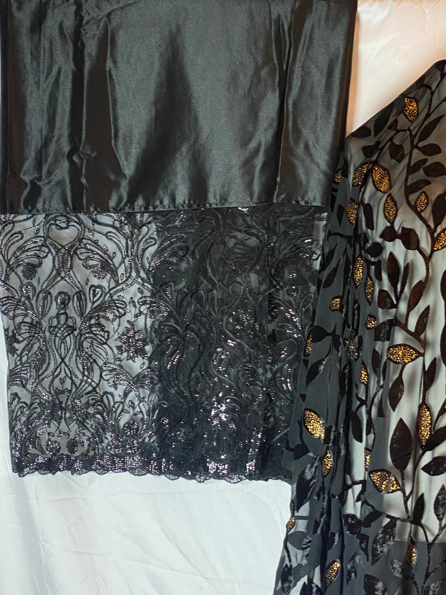 Gorgorad Close-up of black satin fabric with gold floral embroidery on a white background