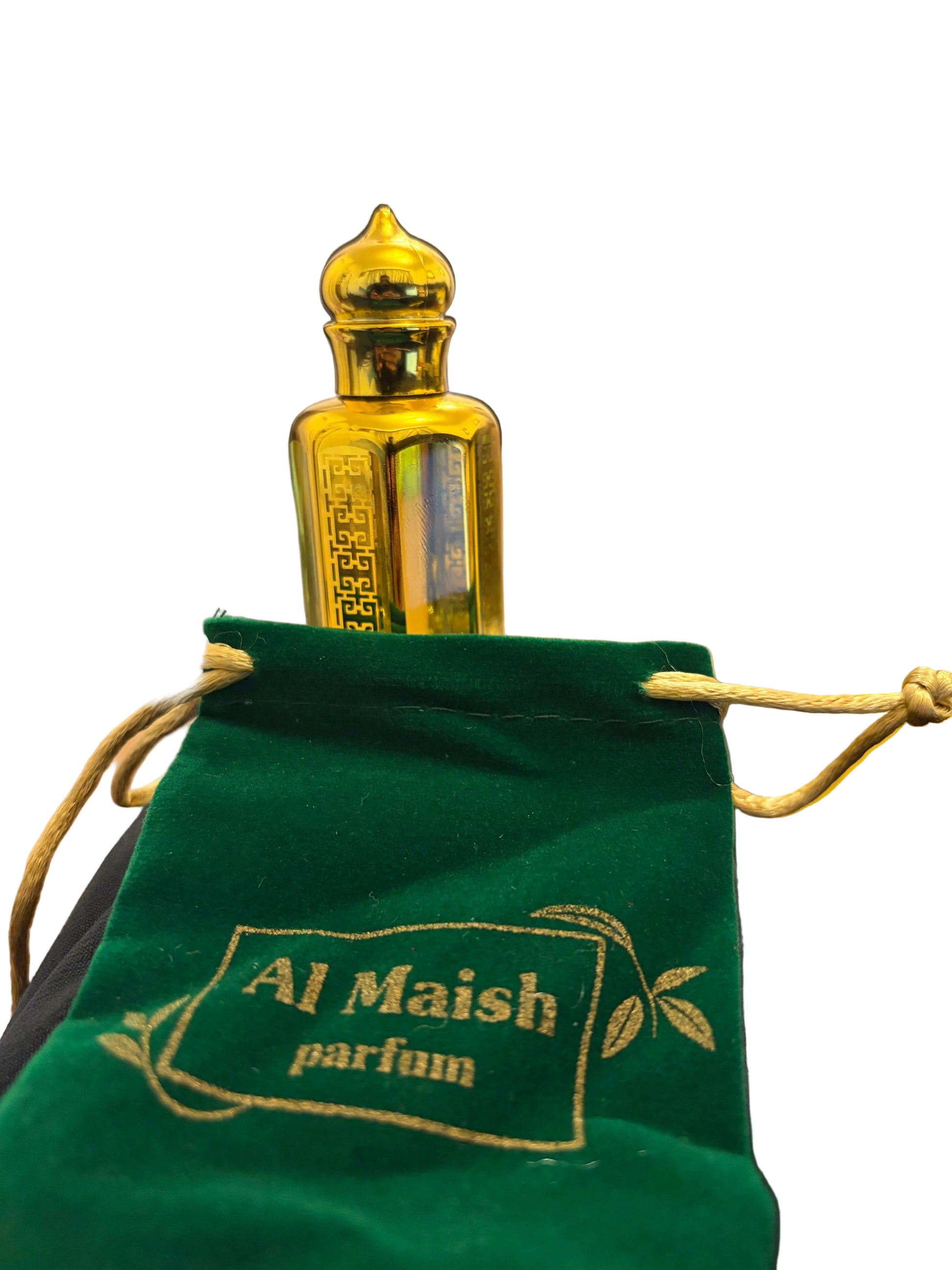 A small ornate gold perfume bottle with a pointed cap stands behind a green velvet drawstring pouch printed with the text 'Al Maish parfum'. The scene is photographed indoors with a blurred home background.