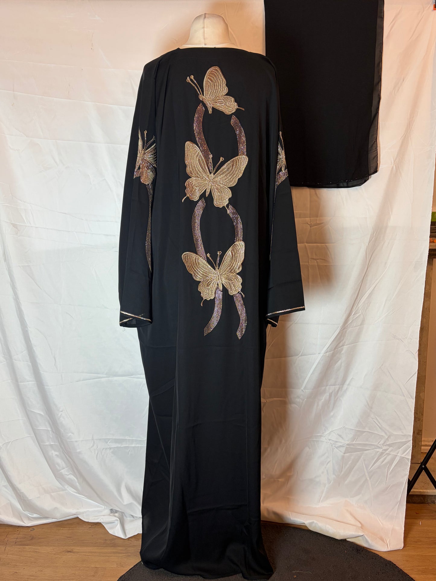 Black dress with butterfly patterns on a mannequin against a white curtain.