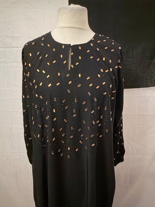 Black dress with gold pattern on a mannequin against a white brick wall.