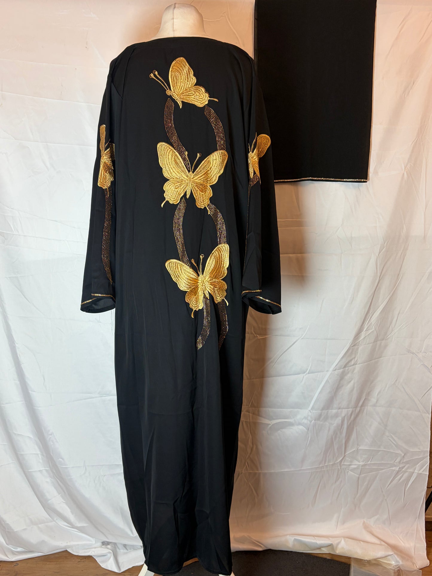 Black abaya dress with gold butterfly designs on a mannequin against a white background