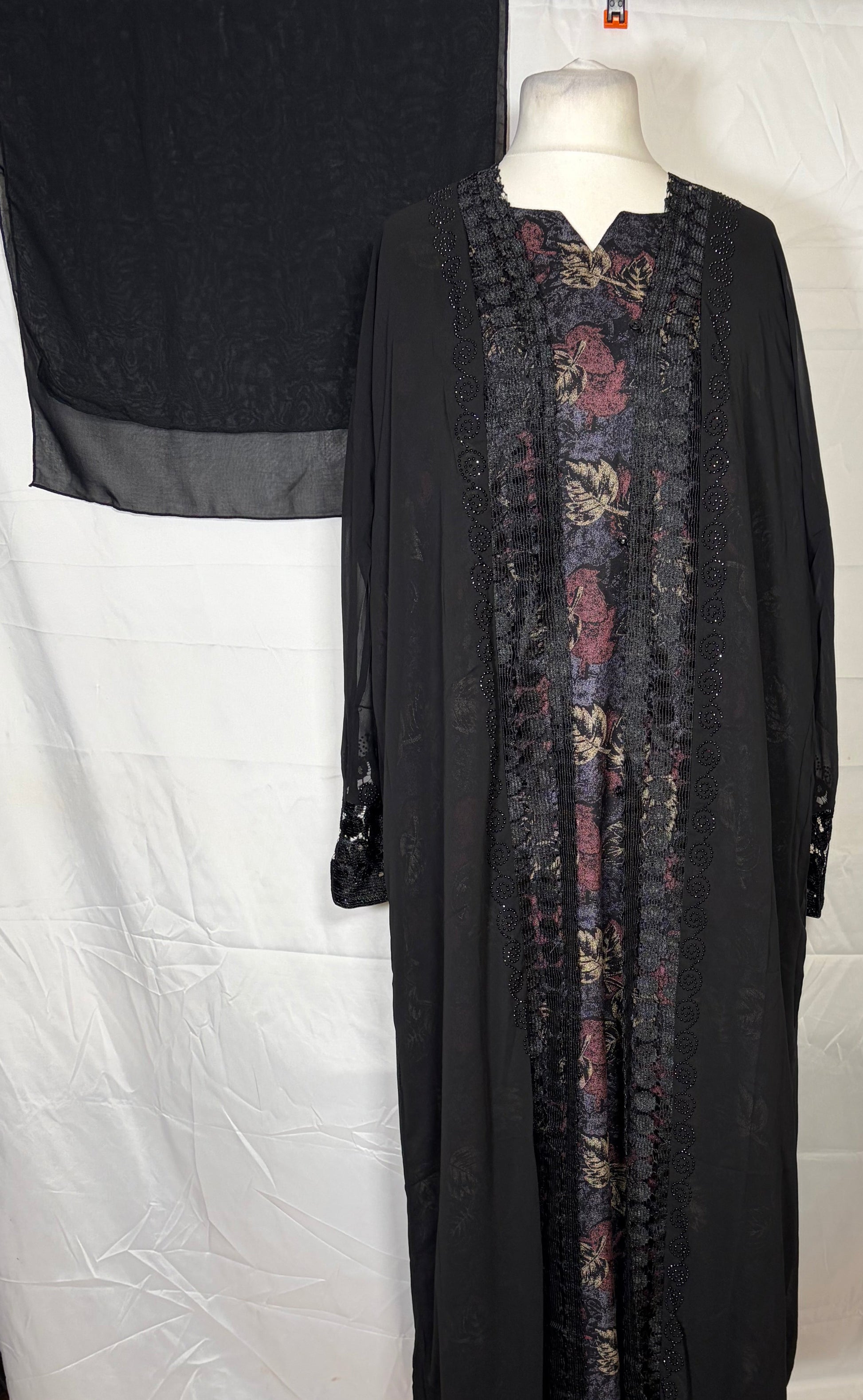 Black abaya with floral patterns on a mannequin against a white backdrop