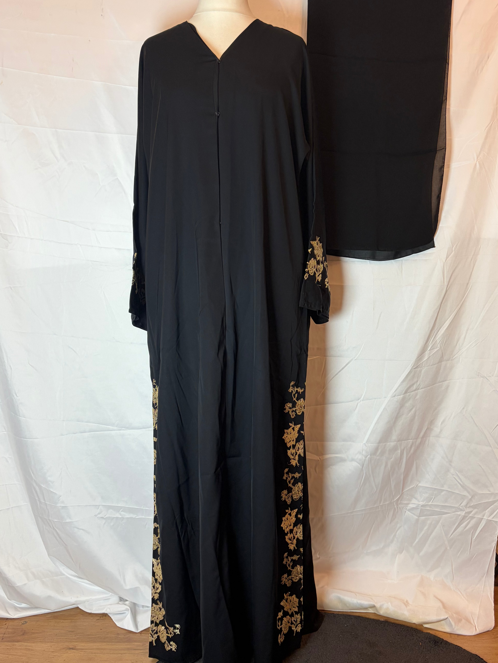 Black Abaya outfit with gold embroidery on a mannequin against a white curtain background