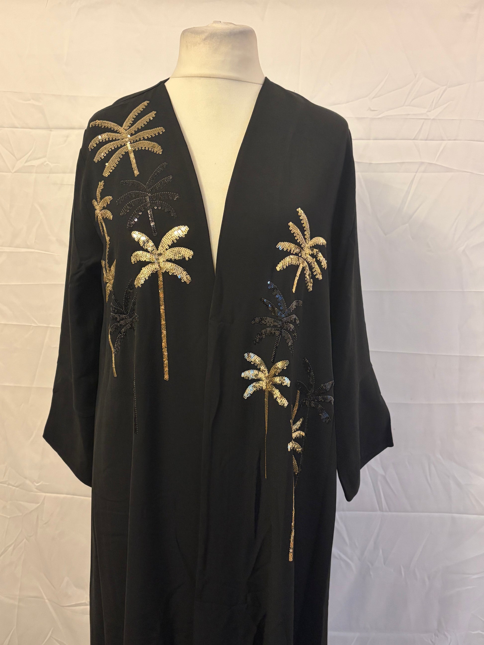 Black dress with gold palm tree embroidery on a mannequin against a white background