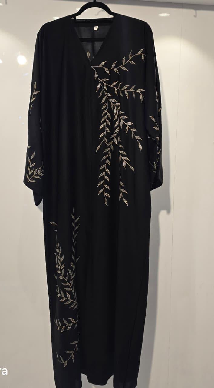 Black dress with leaf patterns on a hanger against a white background