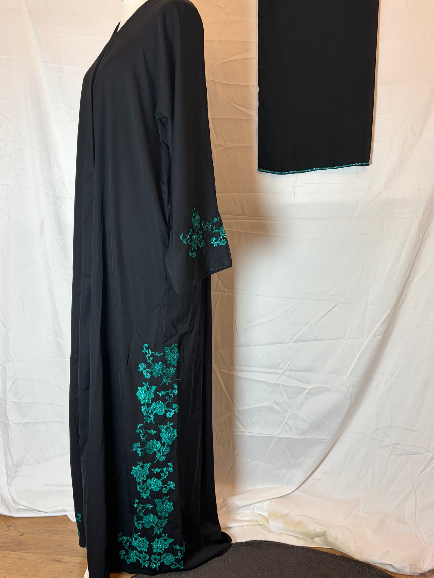 Black garment with green floral embroidery on a white background