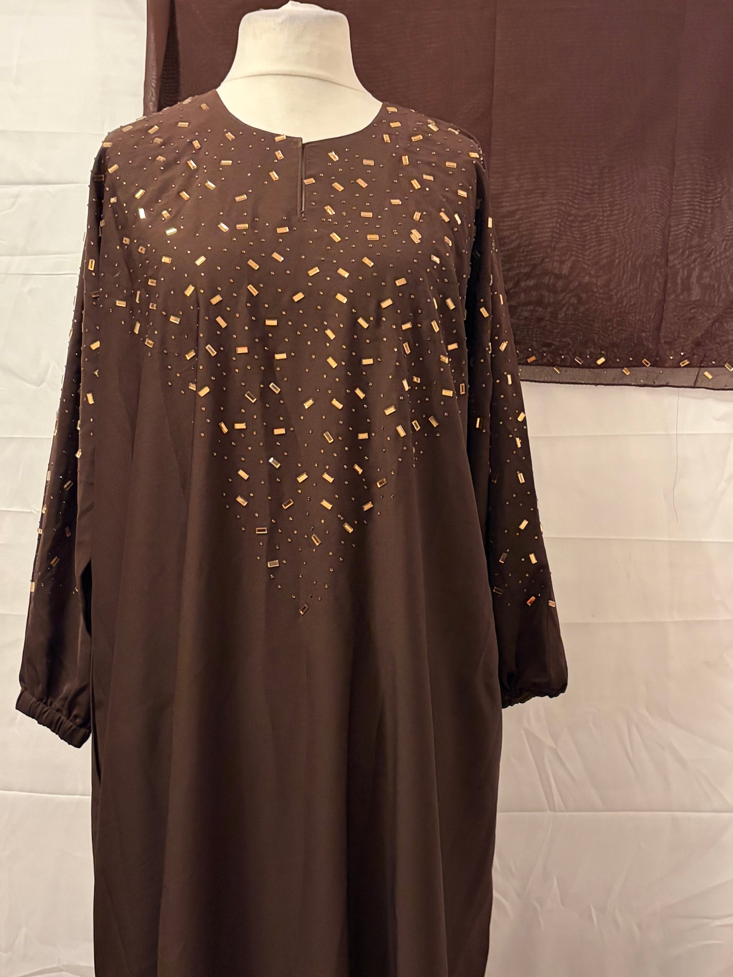 Brown dress with gold patterns on a mannequin against a white background
