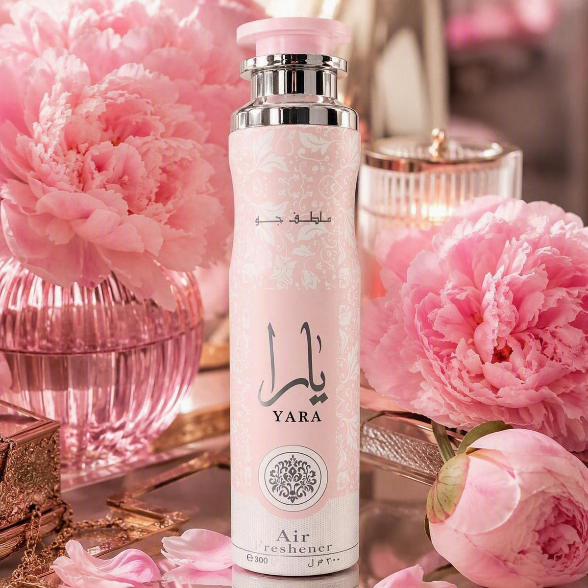 A pink cylindrical air freshener bottle labeled YARA Air freshener, styled with large pink peony flowers and pink glass accessories on a reflective surface.