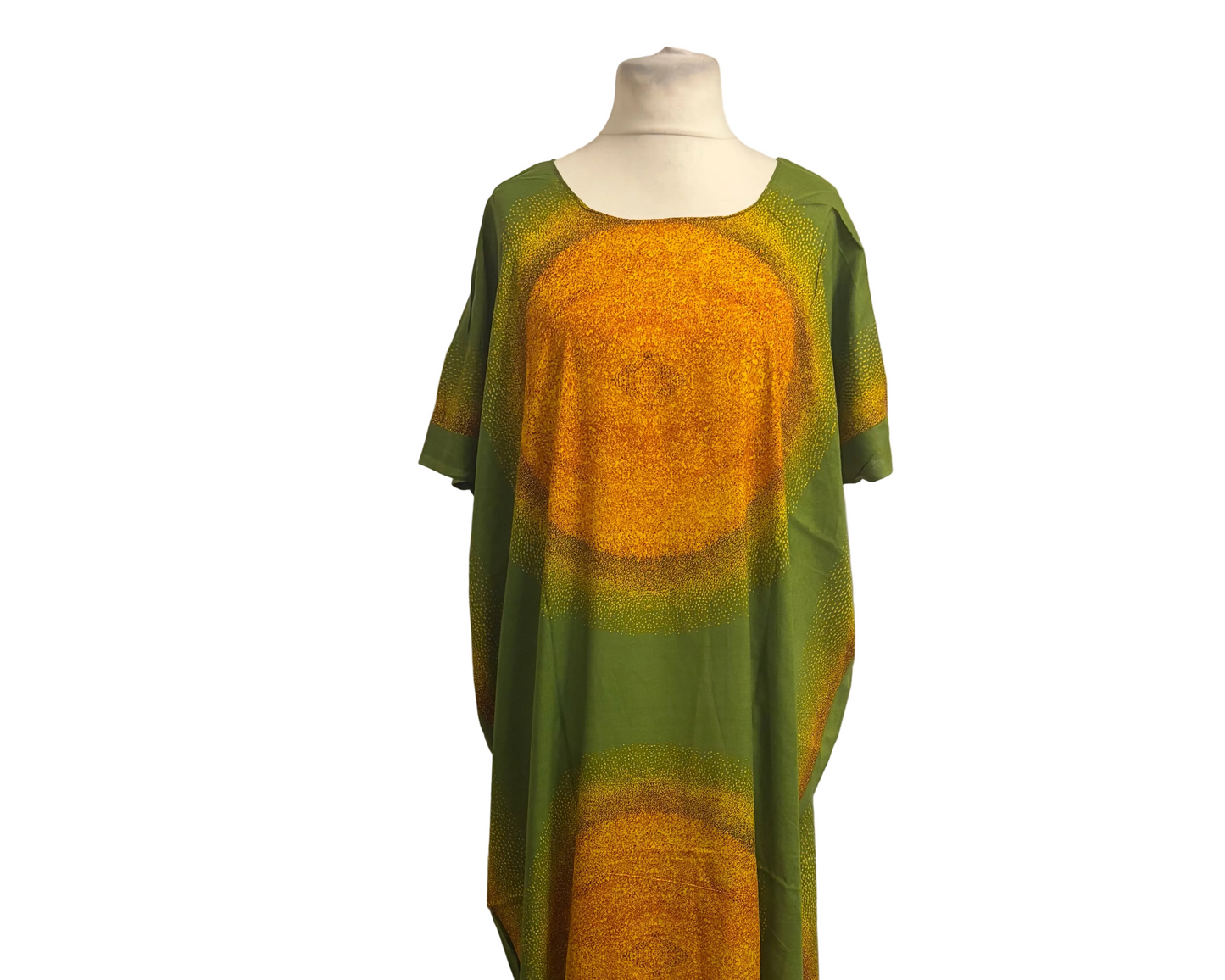 A long, loose Somali baati dress displayed on a mannequin in front of a white fabric backdrop. The garment has a green base with large circular mandala-like patterns in golden yellow and orange.