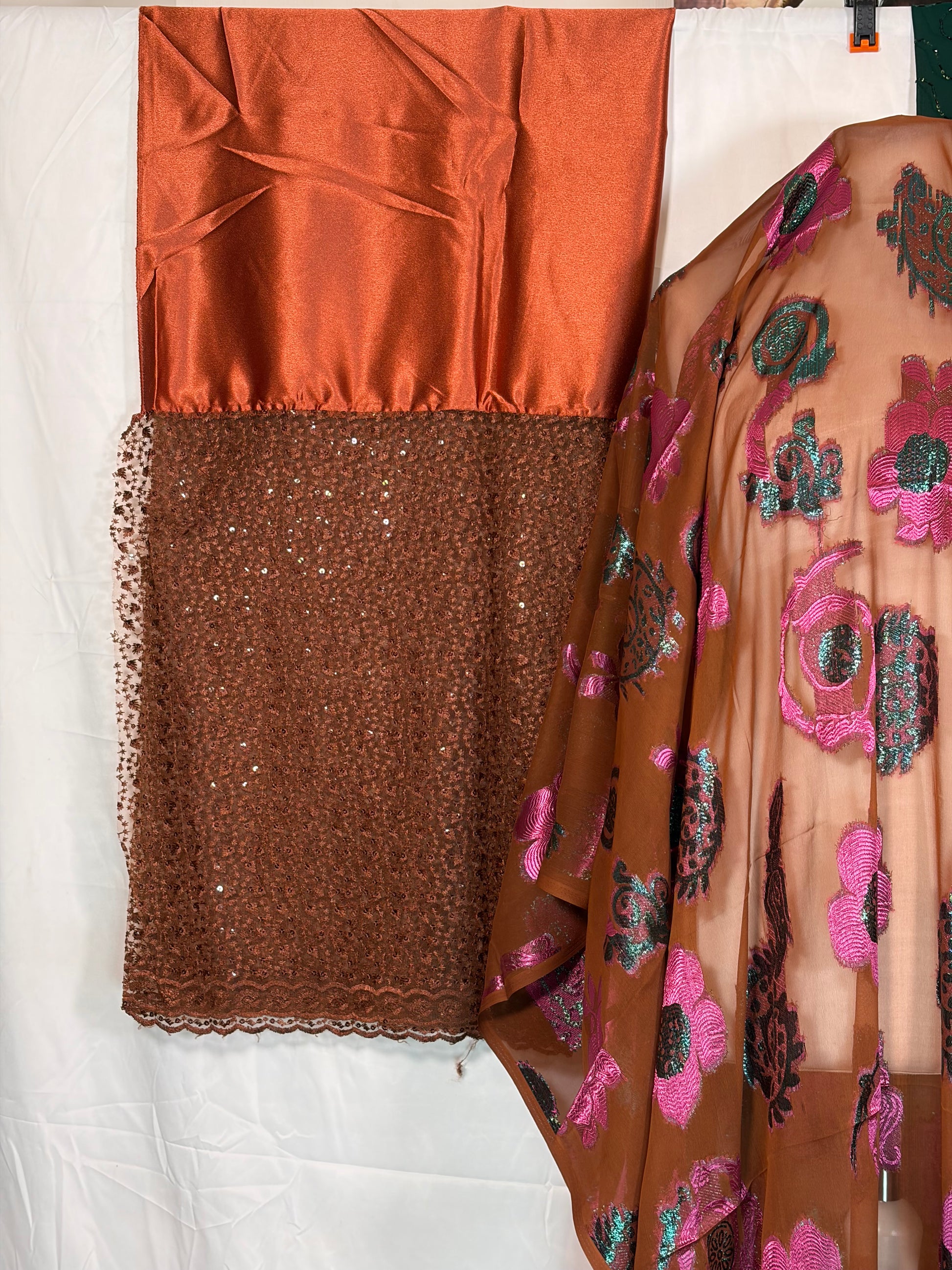 Close-up of fabric with floral pattern, brown satin, and brown textured fabric on a white background