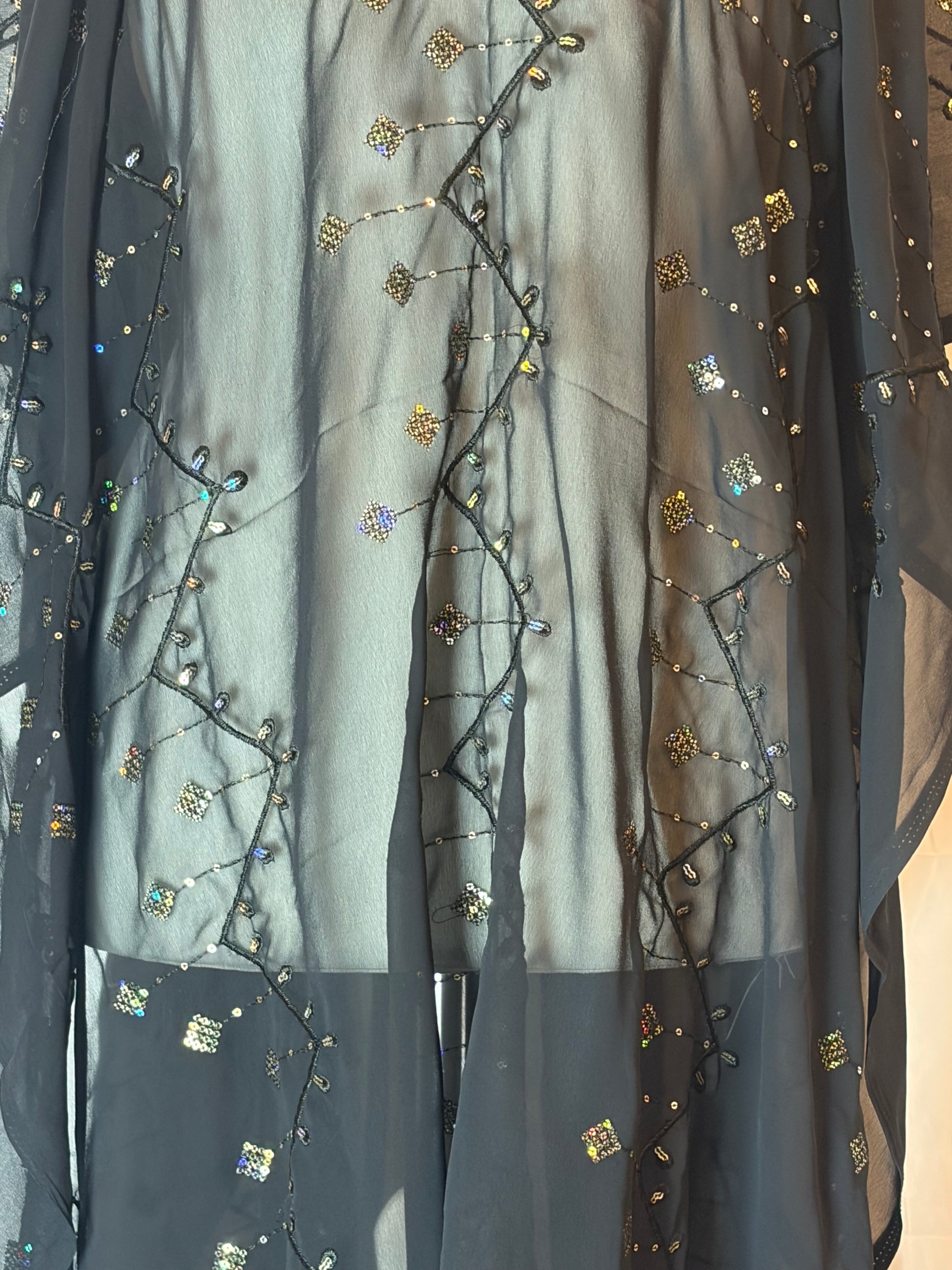 Black Garbasaar fabric with gold embroidery and sequins on a beige background