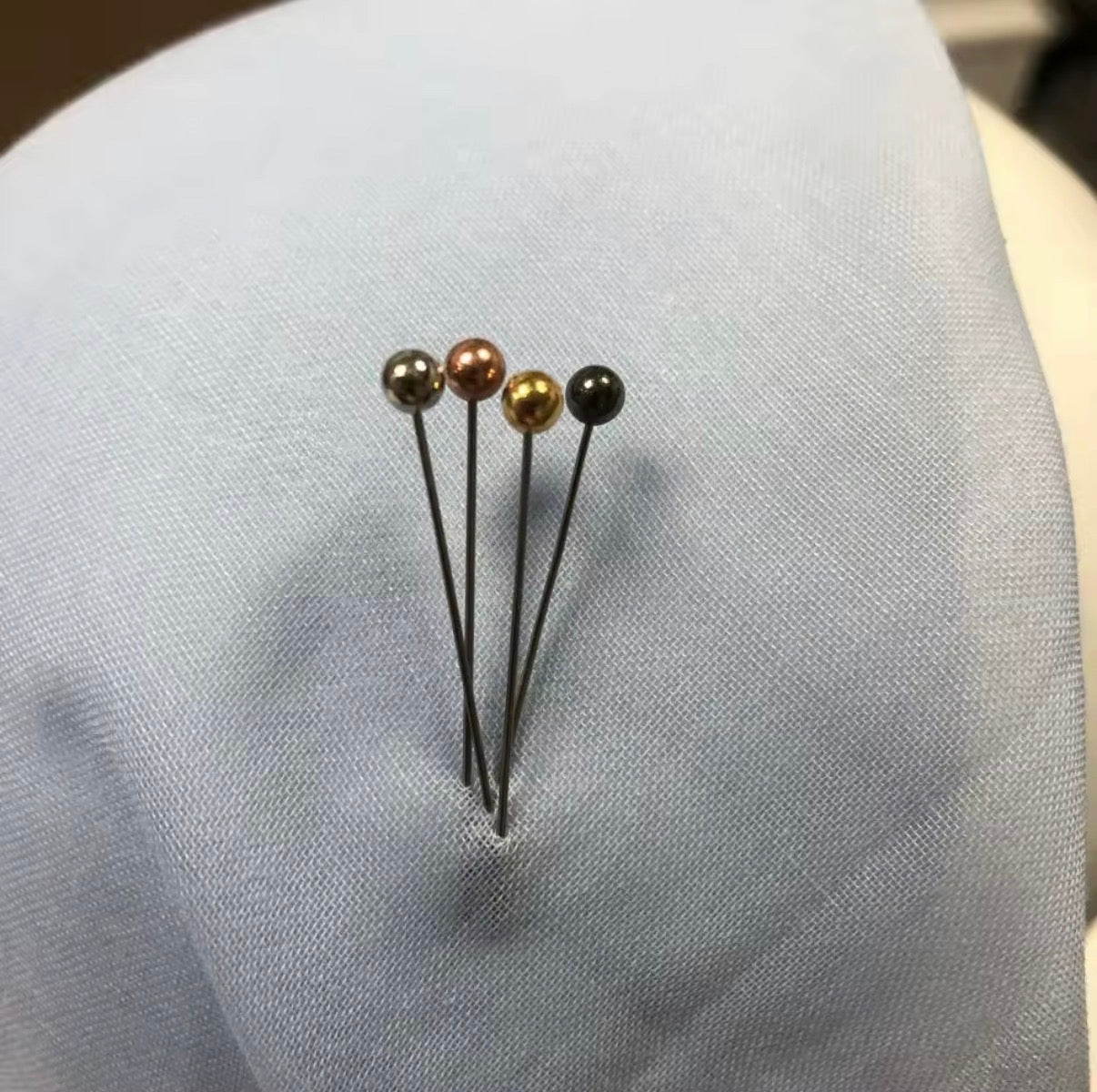 Four pins with different colored beads on a light gray fabric background