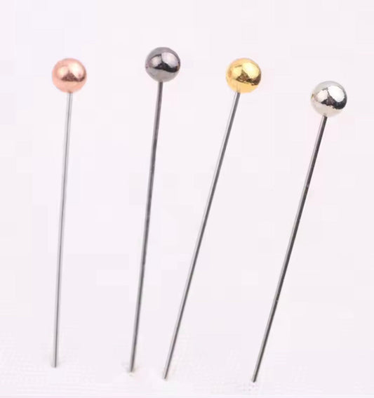 Four metallic Hijab pins with spherical ends on a white background