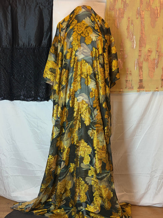 Folded fabric with gold and black floral pattern on a bed