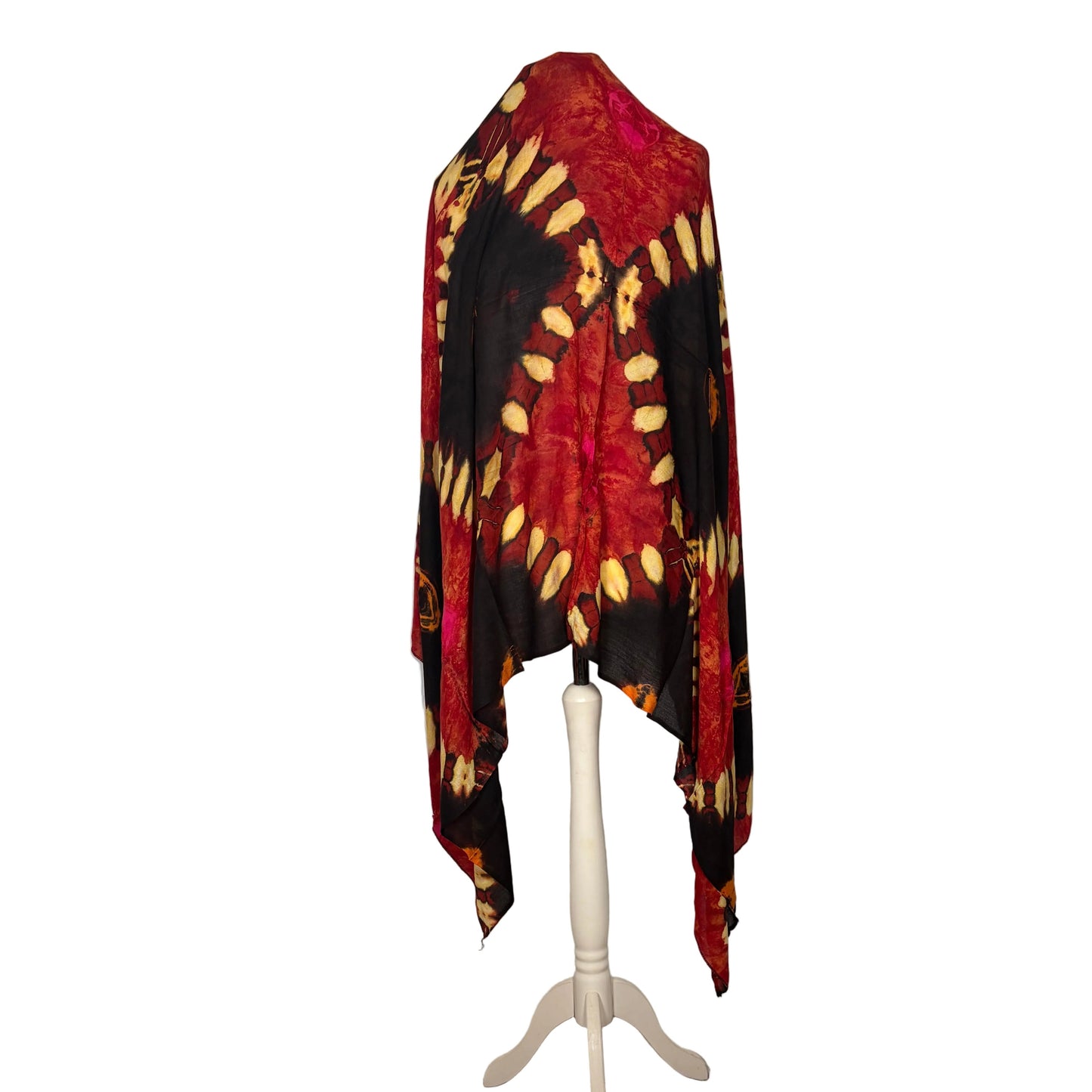 Red, black, and yellow tie-dye shawl on a white mannequin against a white curtain.