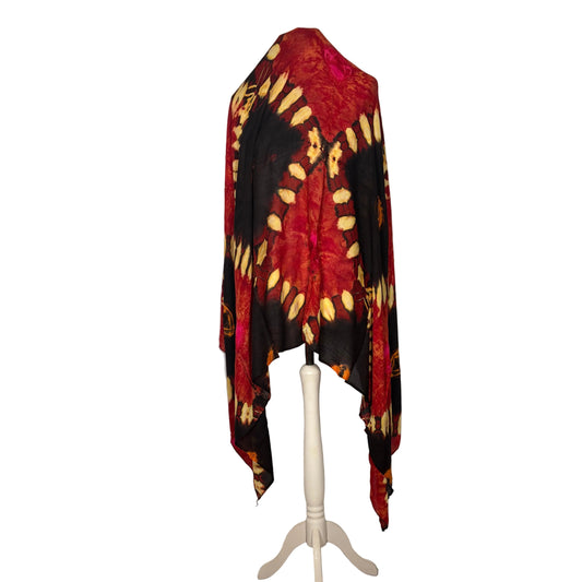 Red, black, and yellow tie-dye shawl on a white mannequin against a white curtain.