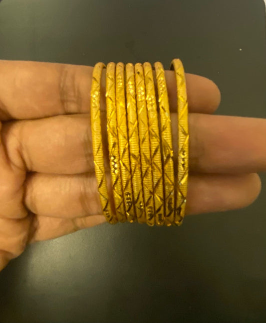 Gold bangles on a hand against a dark background