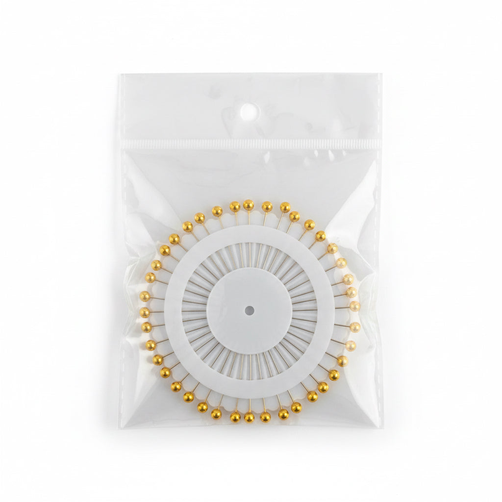 Set of gold-headed Hijab pins on a white card with a clear window, on a wooden surface.
