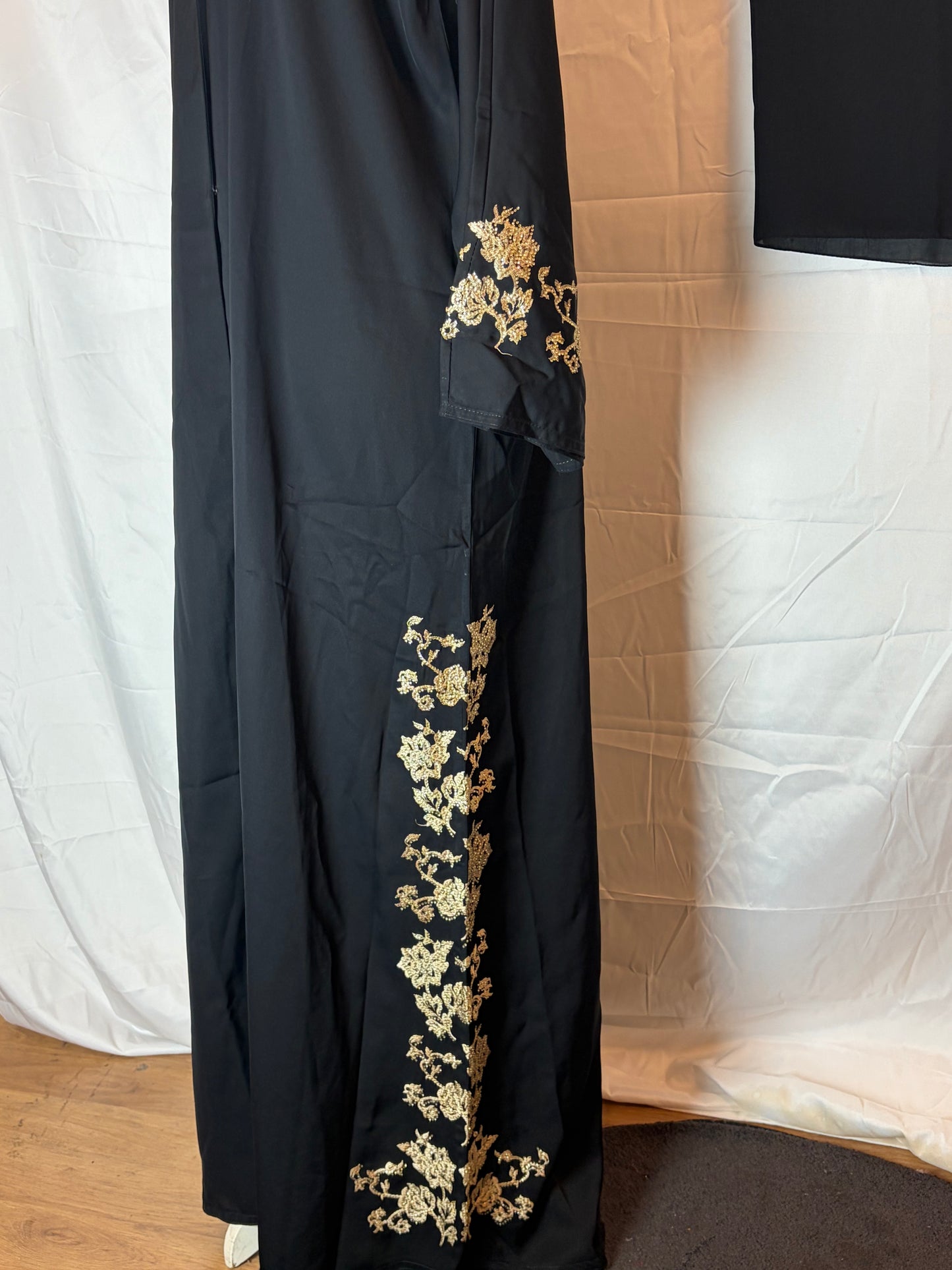 Black garment with gold floral embroidery on a white background