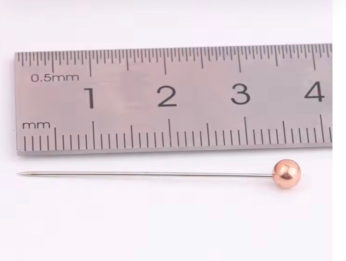 Hijab Pin with a Rose gold pearl tip next to a ruler on a white background