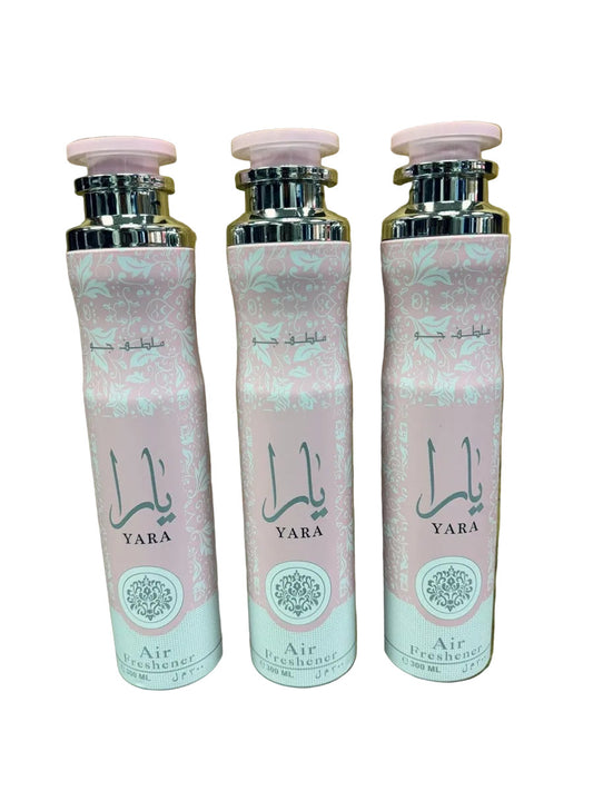 Three YARA Air Freshener bottles with pink and white patterned labels and silver caps, arranged side by side on a reflective surface against a gold textured background.