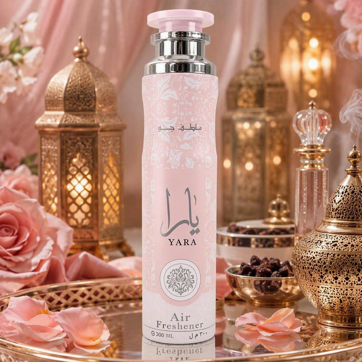 A pink cylindrical air freshener bottle labeled 'YARA' with Arabic text, styled on a reflective tray with pink rose petals, gold lanterns, and warm decorative background elements.