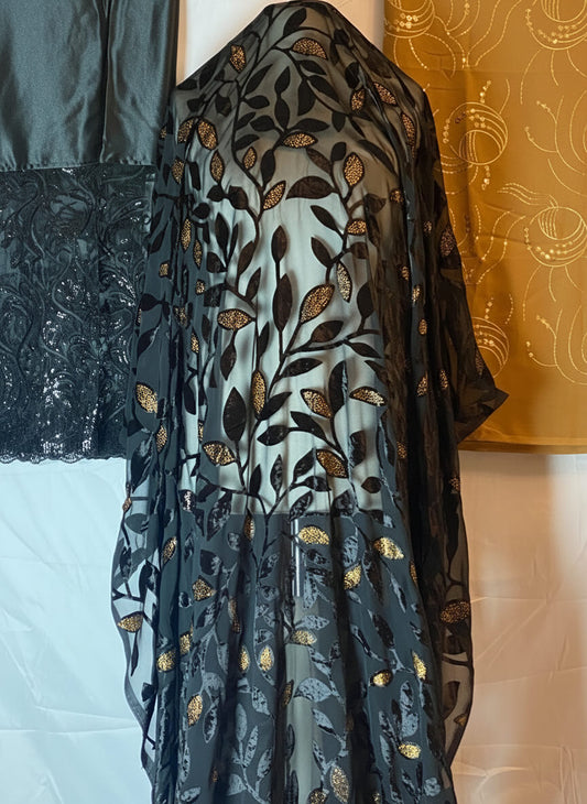 Black floral-patterned sheer dress on a stand against a patterned wall.