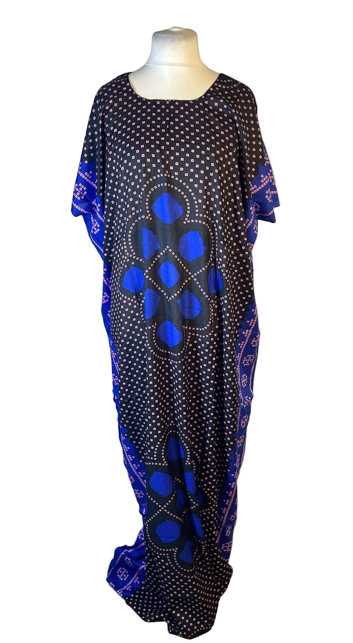 A long black kaftan dress with blue and white polka dots, featuring large blue geometric cutout patterns on the front and blue patterned fabric sleeves and side panels, displayed on a mannequin against a white draped backdrop.