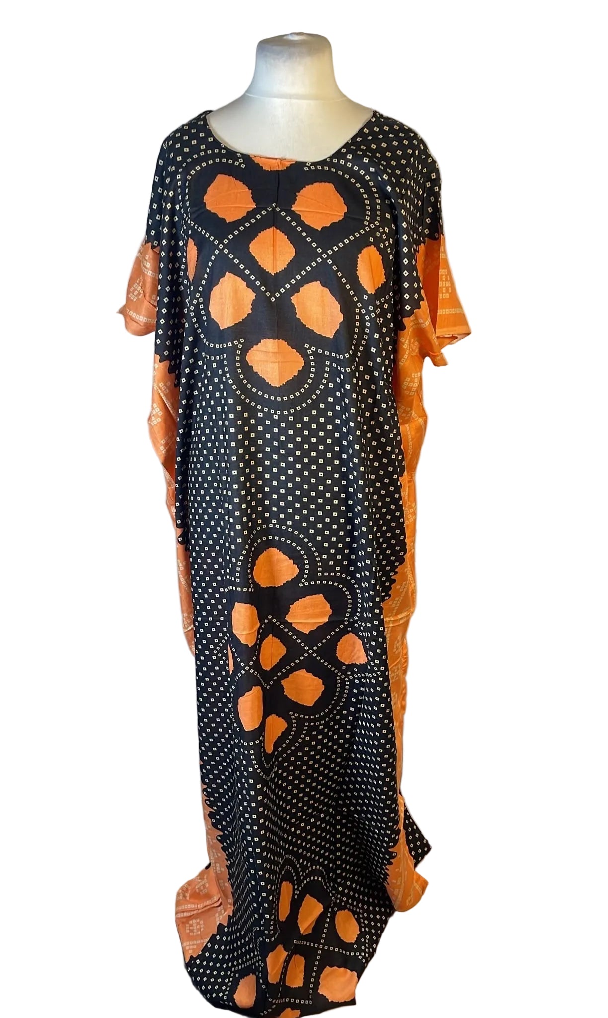 A long black caftan dress with orange and white geometric patterns, displayed on a mannequin against a white fabric backdrop.