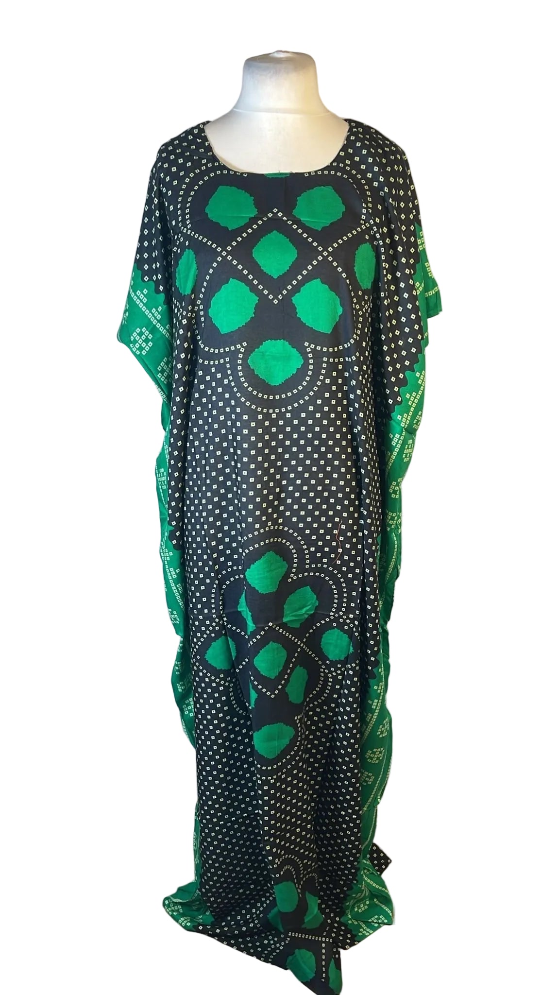 A black caftan dress with green and white geometric patterns displayed on a mannequin against a white fabric backdrop.