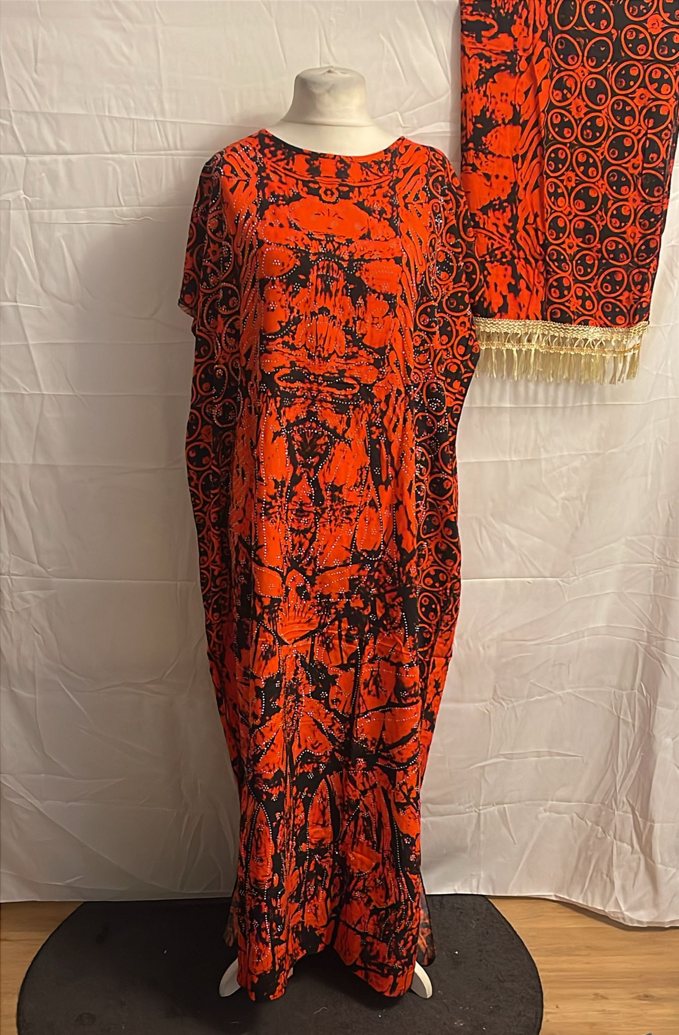 Red and black patterned Somali Baati on a mannequin with a matching scarf draped over it against a white background.