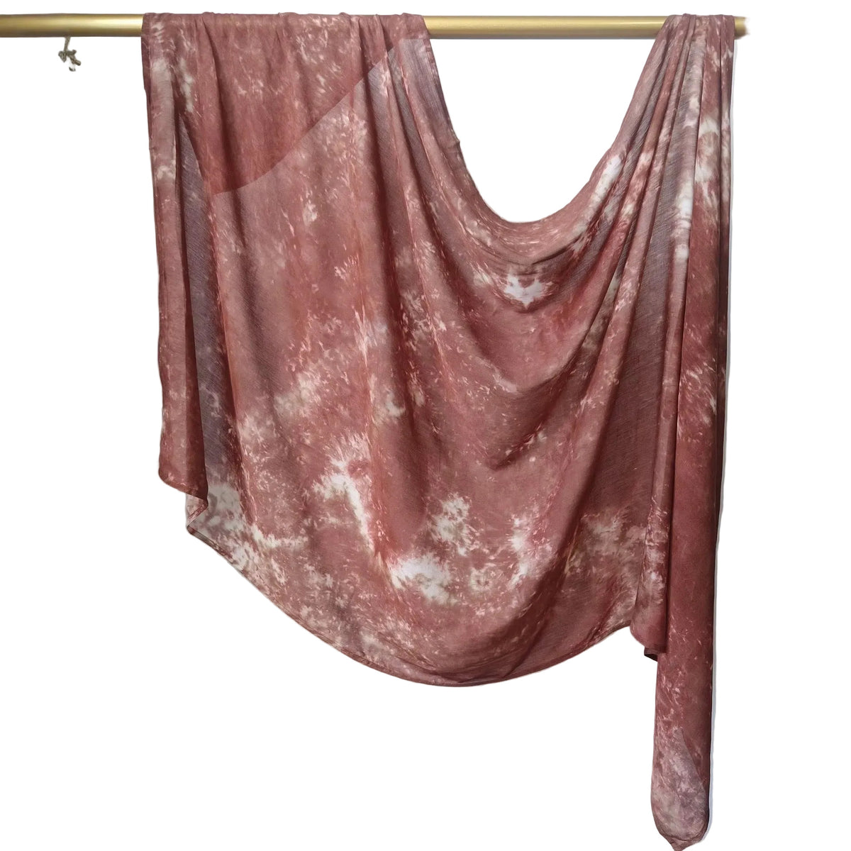 A dusty Brown and white tie-dye shawl draped over a gold metal hanger against a white paneled wall.