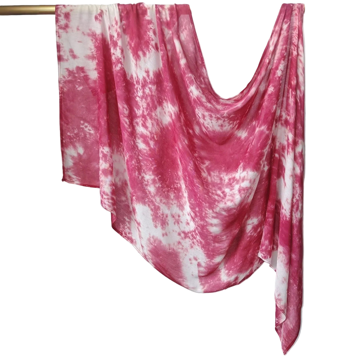 A pink and white tie-dye draped scarf or shawl hanging from a gold-colored clothing rack against a white paneled wall.