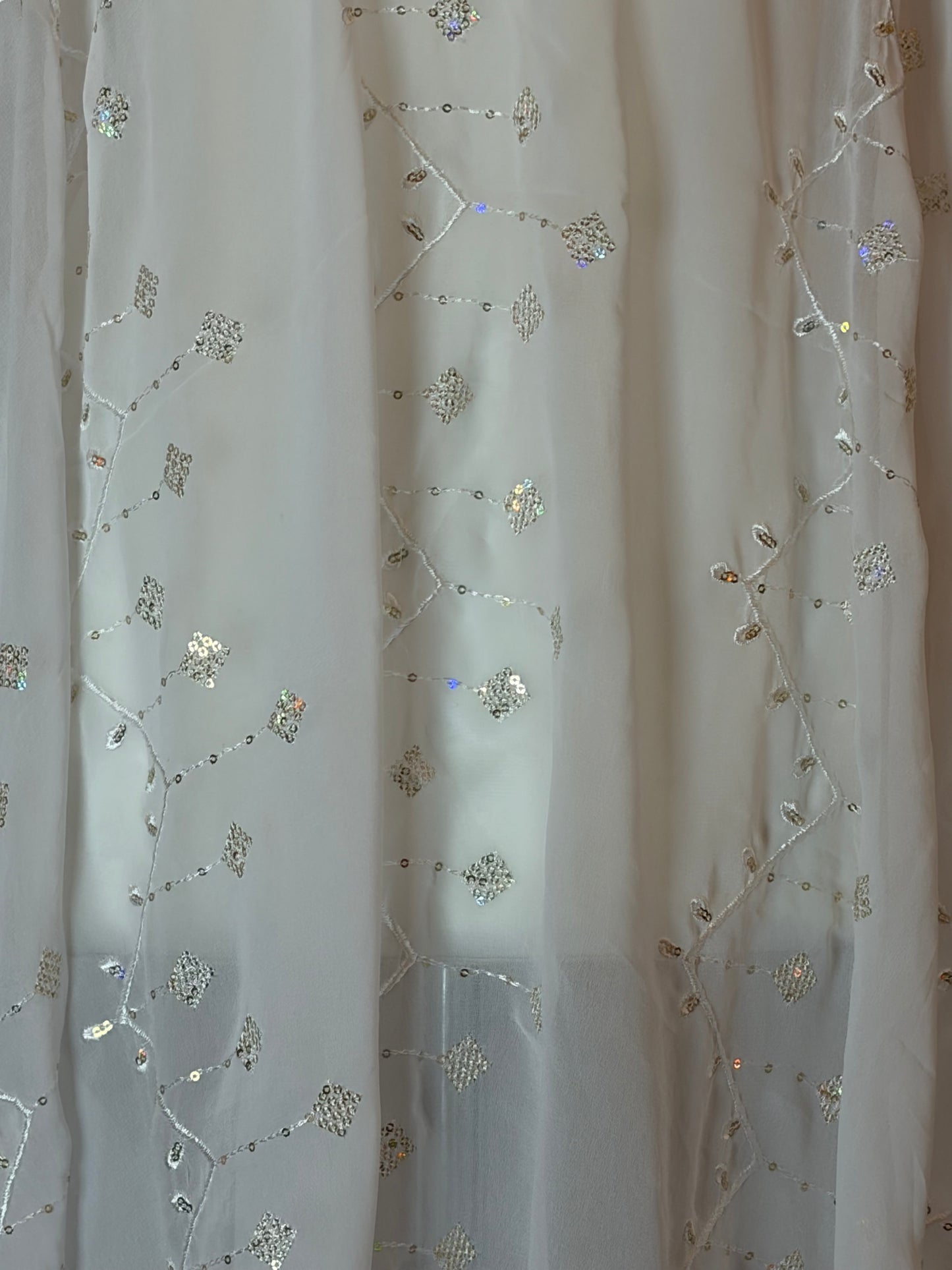 White Garbasaar fabric with floral embroidery and sequins on a wooden surface