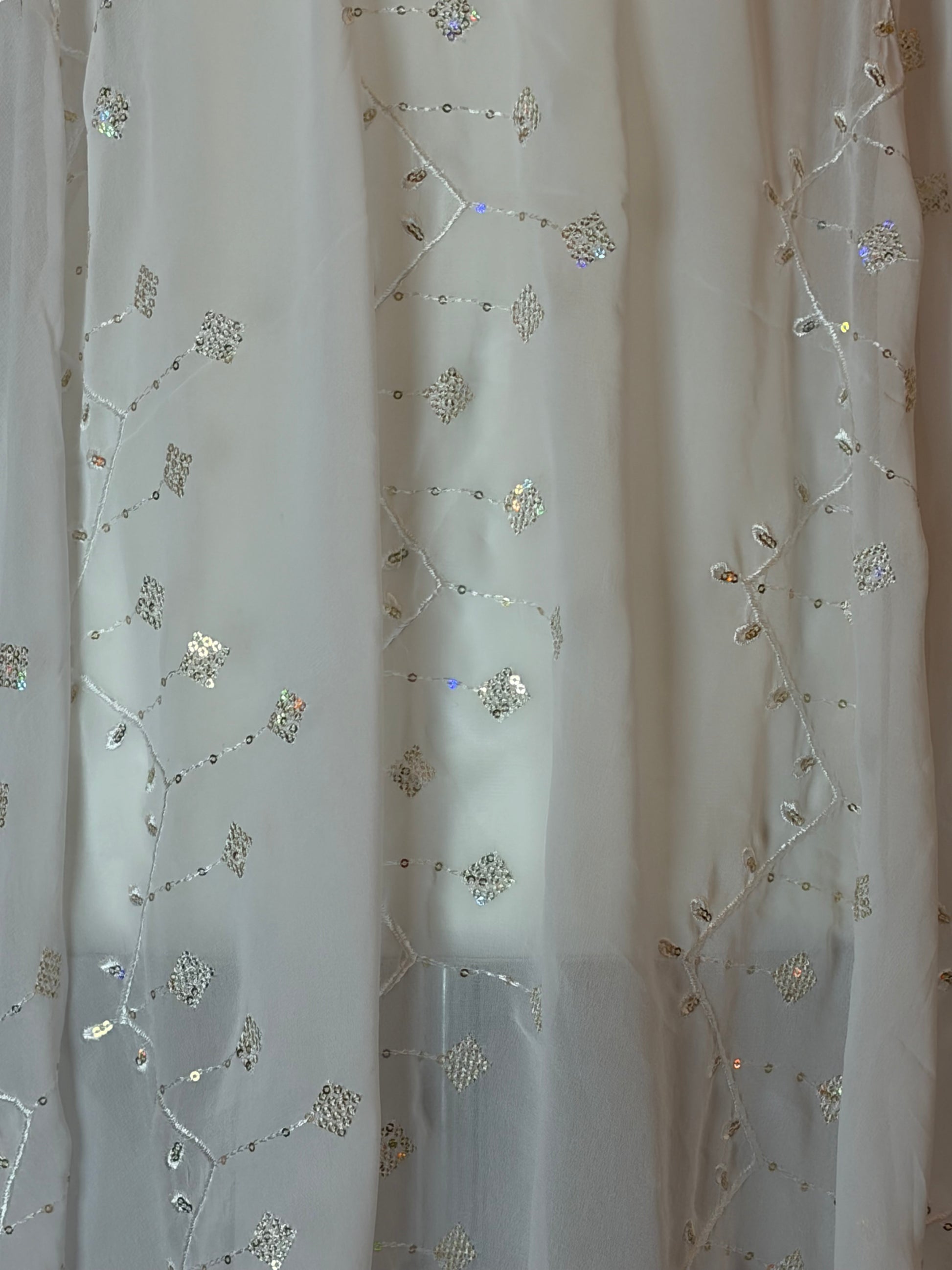 White Garbasaar fabric with floral embroidery and sequins on a wooden surface
