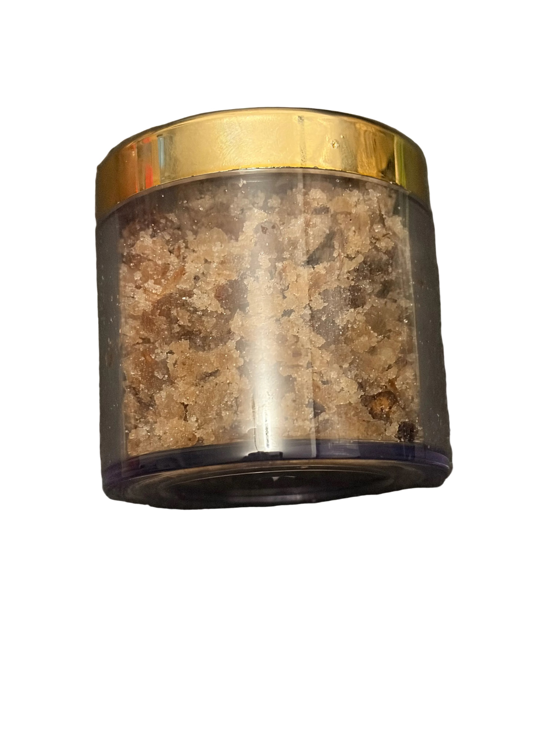 A clear cylindrical plastic jar filled with coarse brown and beige salt crystals, topped with a shiny gold-colored lid, set against a dark gray textured background.